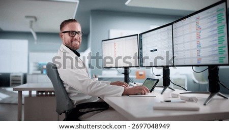 Doctor Smiling While Coding Medical Invoices On Multiple Computer Screens.