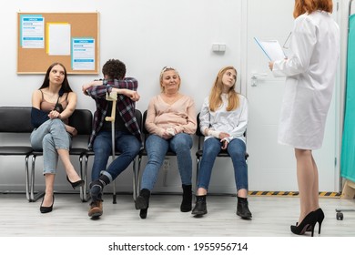 The doctor standing in front of her office reads out the next person and invites them in for a check-up. People of different age are sitting on chairs - Powered by Shutterstock