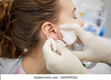 Doctor sterilize piercing place on ear of teenade girl. - Shutterstock ID 1033599262