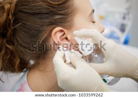 Doctor sterilize piercing place on ear of teenade girl.