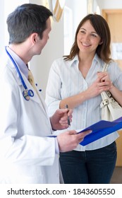 Doctor With A Stethoscope Around His Neck And A Pen In Hand Reviewing A Medical Chart With A Female Patient In The Corridor