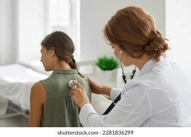 Doctor with a stethoscope examining a child patient. Female doctor in a white coat examining the lungs of a teenage girl. Healthcare, clinic, medical checkup concept - Powered by Shutterstock