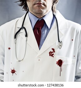 Doctor With Stethoscope In White Coat With Red Bloody Stains Over It And Very Dramatic Side Light And Harsh Shadows.