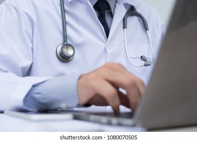 Doctor With Stethoscope Working On Laptop Computer, Typing On Keyboard, Browsing Internet Or Reviewing Medical Record. Telemedicine, Teleconference, E Health, Medical Online Concept. Close Up