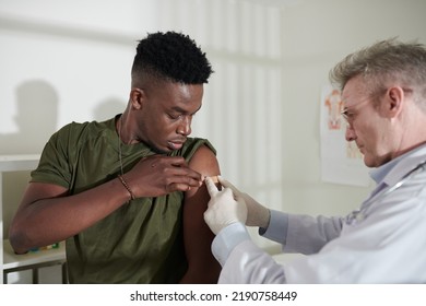 Doctor Sticking Adhesive Bandage On Vaccine Injection Site On Arm Of Soldier