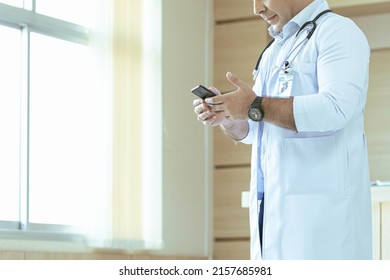 The Doctor Stood And Looked At His Smartphone Before Entering The Emergency Room To Examine The Patient.