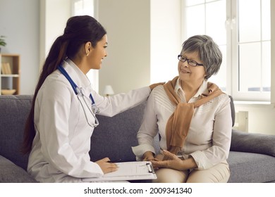 Doctor Supporting, Comforting And Reassuring Her Senior Patient During Her Home Visit. Happy Mature Woman Sitting On Couch In Living-room Listening To Family Physician Or General Practitioner's Advice