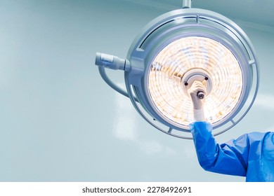 Doctor or surgeon in blue gown holding surgical lamp to adjust light inside operating theatre with space in background.People did surgery in hospital.Nurse with medical glove in operating room. - Powered by Shutterstock