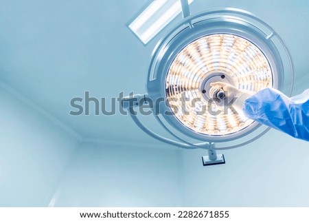 Doctor or surgeon in blue gown holding surgical lamp to adjust light inside operating theatre with space in background.People did surgery in hospital.Nurse with medical glove in operating room.