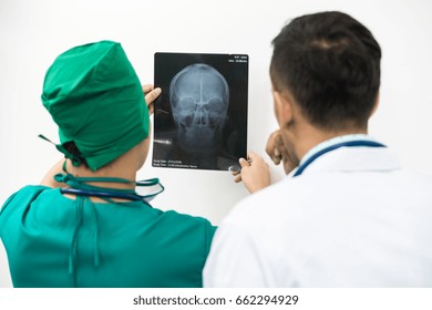 Doctor And Surgeon Examining X-ray Film Of Patient 's Head For Brain, Skull Or Eye Injury. Medical Diagnosis And Surgical Treatment Concept. 