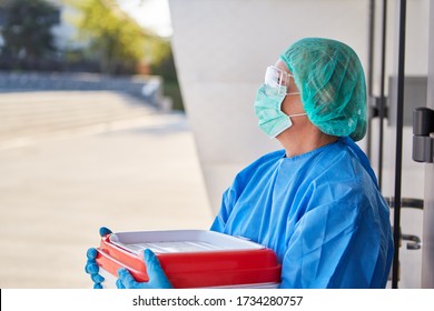 Doctor Or Surgeon In Organ Transport For Surgery In Front Of The Clinic In Protective Clothing Pauses At The Door