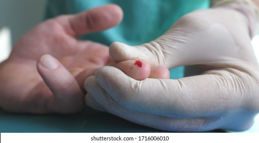 Doctor takes blood sample from finger of patient for test to COVID-19. Hands of medic in protective gloves pricks finger of man with a needle to take analysis to coronavirus during pandemic. Close up.