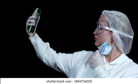 Doctor Takes Out A Smartphone, Takes Off The Mask From His Face And Takes A Selfie On A Black Background