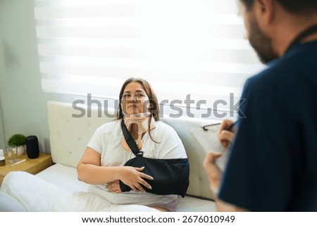 Doctor taking notes while visiting a recovering patient wearing neck brace and arm sling in bedroom at home