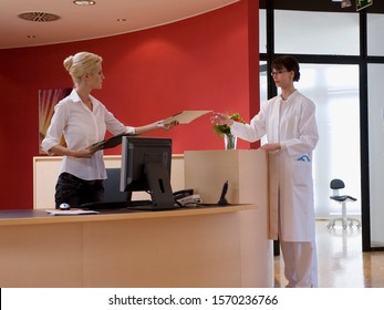 Doctor Taking Paperwork From Receptionist In Office