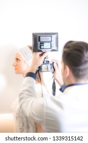 Doctor Taking Picture Of The Face Of Young Female Patient Before Plastic Surgery On White Background.