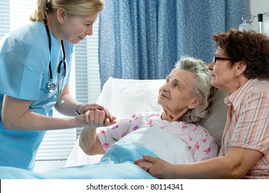 Doctor Talking To Elderly Patient Lying In Bed In Hospital