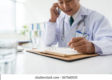 Doctor Talking On The Phone And Making Notes In His Notepad