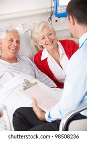 Doctor Talking To Senior Couple On UK Hospital Ward