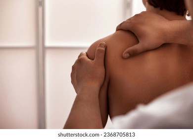 Doctor therapist doing wellness shoulder massage for sporty male, hands massaging body, close up. Handsome athletic man visit masseur in medical room, inside. Rehab massage concept. Copy ad text space