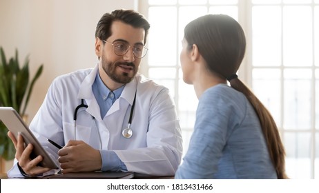 Doctor therapist gp wearing white uniform with stethoscope consulting young woman patient at meeting, using computer tablet, giving recommendations, explaining medical checkup results