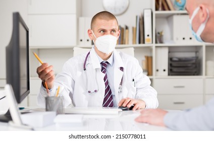 Doctor Therapist Male In Face Mask Shows The Patient The Results Of His Tests And Prescribes Treatment In A Modern Office In The Hospital