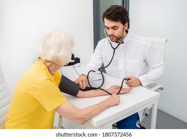 Doctor Therapist In Modern Clinic Measures Body Pressure Of An Senior Woman. Prevention Of Diseases Of Hypertension, Atherosclerosis And Heart Failure