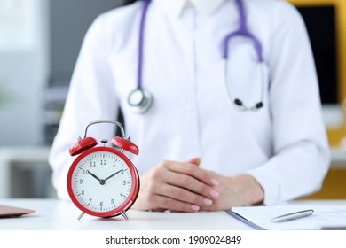 Doctor Therapist Sitting In Office In Front Of Red Alarm Clock Closeup. Doctors Schedule Concept