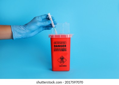 Doctor throwing used syringe into sharps container on light blue background, closeup