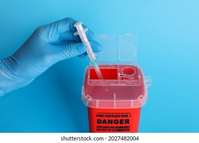 Doctor throwing used syringe into sharps container on light blue background, closeup - Shutterstock ID 2027482004