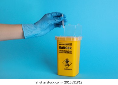 Doctor throwing used syringe needle into sharps container on light blue background, closeup - Shutterstock ID 2015531912