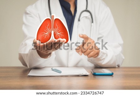 A doctor in a uniform holding a lung shape symbol while sitting at a table in the hospital. World tuberculosis day, world no tobacco day, lung cancer, pulmonary hypertension, pneumonia.