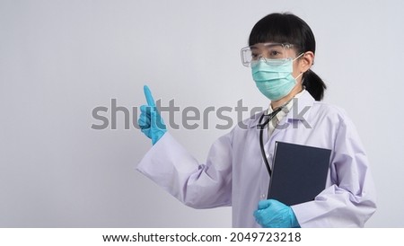 Doctor in uniform points to an empty area. Wearing blue medical latex gloves and clear goggles and green N95 mask to prevent epidemic virus. Asian doctor. Hand gesture. Medical stethoscope. Virus book