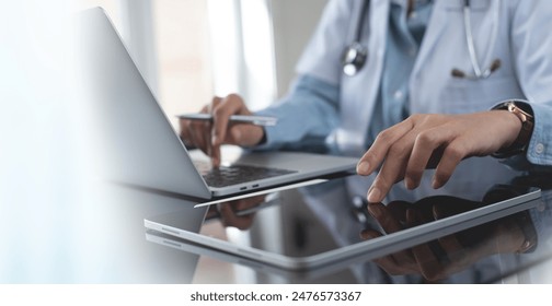 Doctor using digital tablet and working on laptop computer at doctor's office in hospital, close up. Healthcare and medicine, medical technology background - Powered by Shutterstock