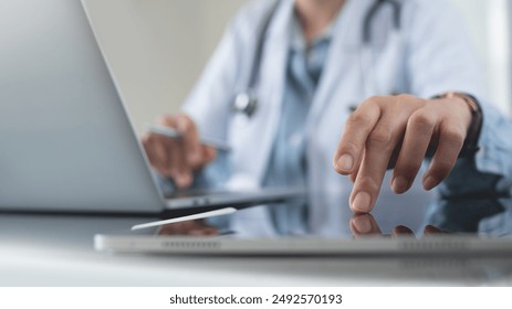 Doctor using digital tablet and working on laptop computer at doctor's office in hospital, close up. Healthcare and medicine, medical technology background