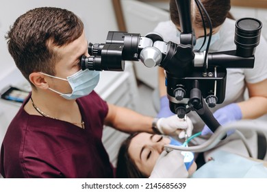 The Doctor Is Using Equipment To Help The Patient. He Is Using A Dental Equipment. It Is Used To Find The Problem With The Patient's Teeth. The Dentist Is Wearing Dark Purple Medical Shirt, Blue Mask.