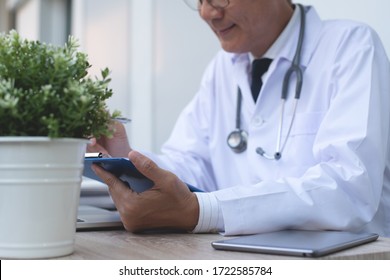 Doctor Using Mobile Smartphone For Zoom Online Meeting Apps, Reviewing Patient's Information, Writing Prescription And Working On Laptop Computer In Medical Office In Hospital, Close Up