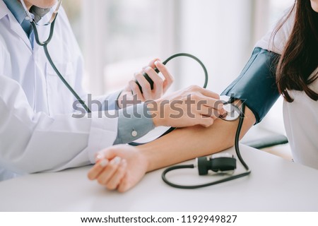 Doctor using sphygmomanometer with stethoscope checking blood pressure to a patient in the hospital.