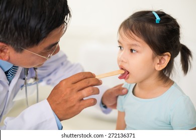 Doctor Using Tongue Depressor To Check Throat Of A Girl