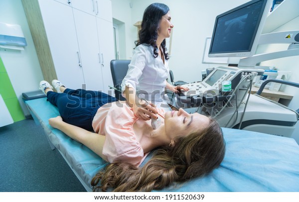 Doctor using ultrasound scanning machine for\
examining a thyroid of\
woman