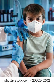 Doctor Vaccinating Child In The Pediatric Clinic. Child Wearing Mask Getting Vaccinated By Pediatrician Holding A Syringe