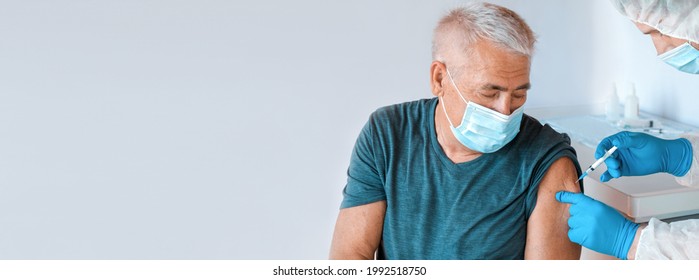 Doctor Vaccinating Senior Man In Clinic. Elderly People Vaccination. Doctor Giving COVID 19 Coronavirus Vaccine Injection To Mature Man In Face Mask. Protection Of Senior Patient. Old Man In Hospital
