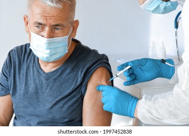 Doctor Vaccinating Senior Man In Clinic. Elderly People Vaccination. Doctor Giving COVID 19 Coronavirus Vaccine Injection To Mature Man In Face Mask. Protection Of Senior Patient. Old Man In Hospital