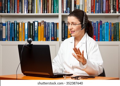 Doctor or vet sitting with a headset or headphones at her desk in front of a computer with an attached camera, talking soothingly with a patient, telemedicine concept