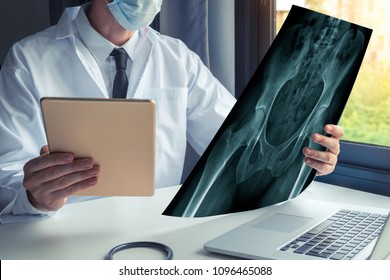 Doctor Watching A X-ray Of Bones Of Hips And Holding A Digital Tablet With Laptop