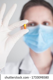 Doctor Wearing Blue Face Medical Mask And Clear Latex Gloves Holding Tablet Pill On Grey Hospital Wall Background. Antibiotics And Virus Treatment Tablet.