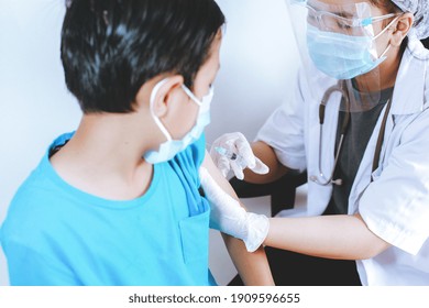 Doctor Wearing Complete PPE With Syringe Needle Inject To Boy Patient. Medicine, Vaccination, Immunization And Health Care Concept