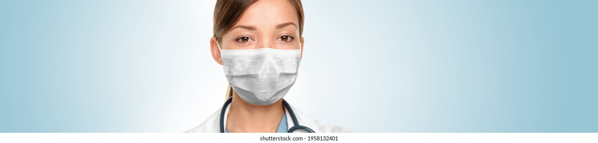 Doctor wearing face mask PPE as coronavirus spreading prevention at hospital banner. Panoramic portrait of serious ethnic Asian medical healthcare professional, blue background.