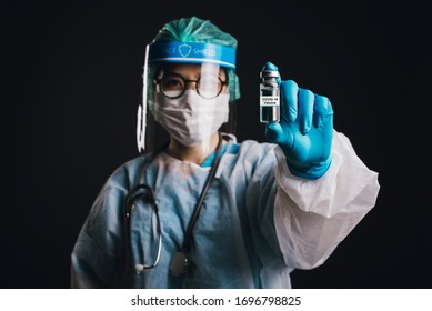 Doctor Wearing Face Shield And PPE Suit For Coronavirus Outbreak (Covid-19) Holding Showing Covid-19 Vaccine On Black Background, Concept Of Covid-19 Quarantine.