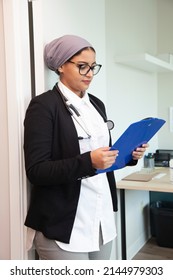 A Doctor Wearing A Hijab And Stethascope Looks At A Medical Chart In Her Office